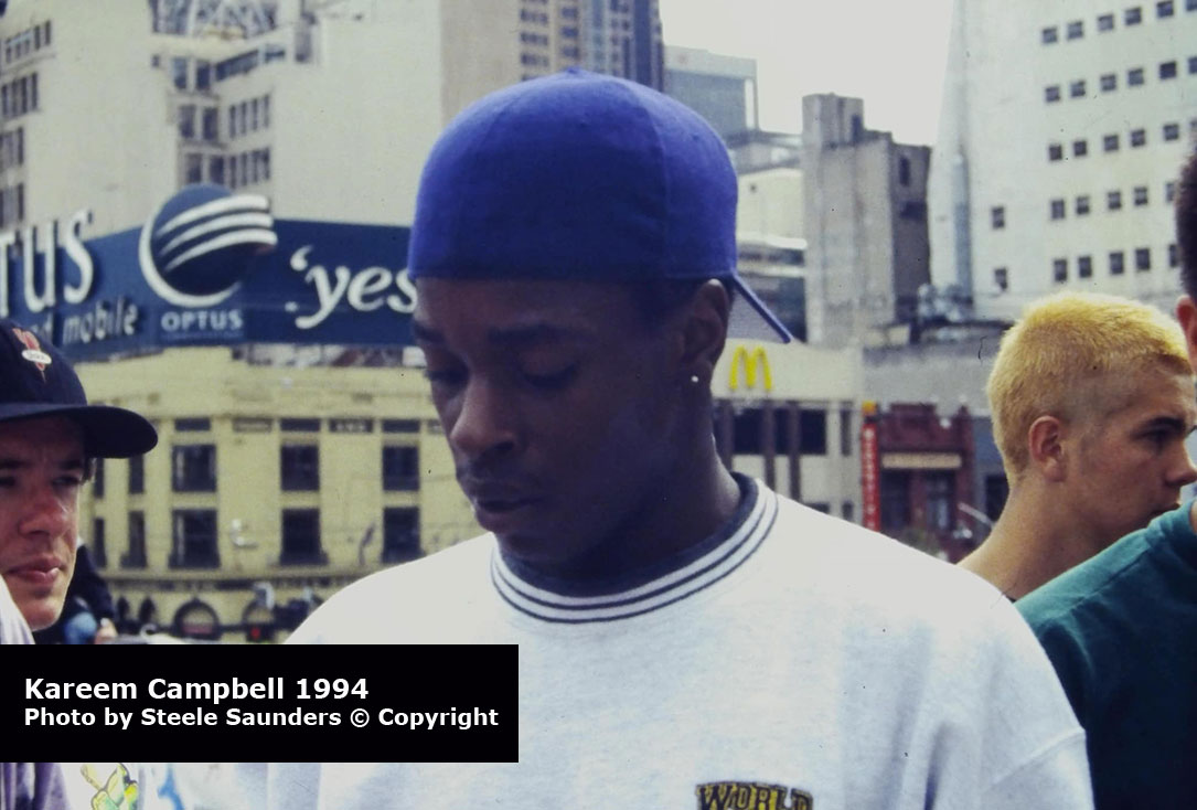 Portrait of Kareem Campbell wearing a baseball cap backwards
            and a World Industries embroidered sweater. The photograph was taken by Steele Saunders in 1994