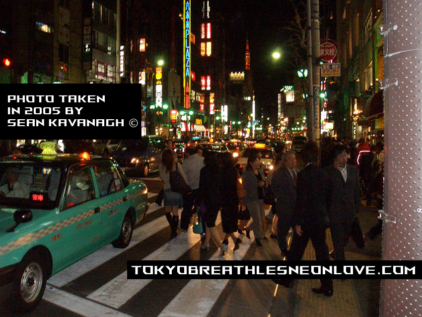 Photo of the main street in Roppongi on a busy weeknight. 
    A crowd of people are crossing the road with colorful neon lights in the background.